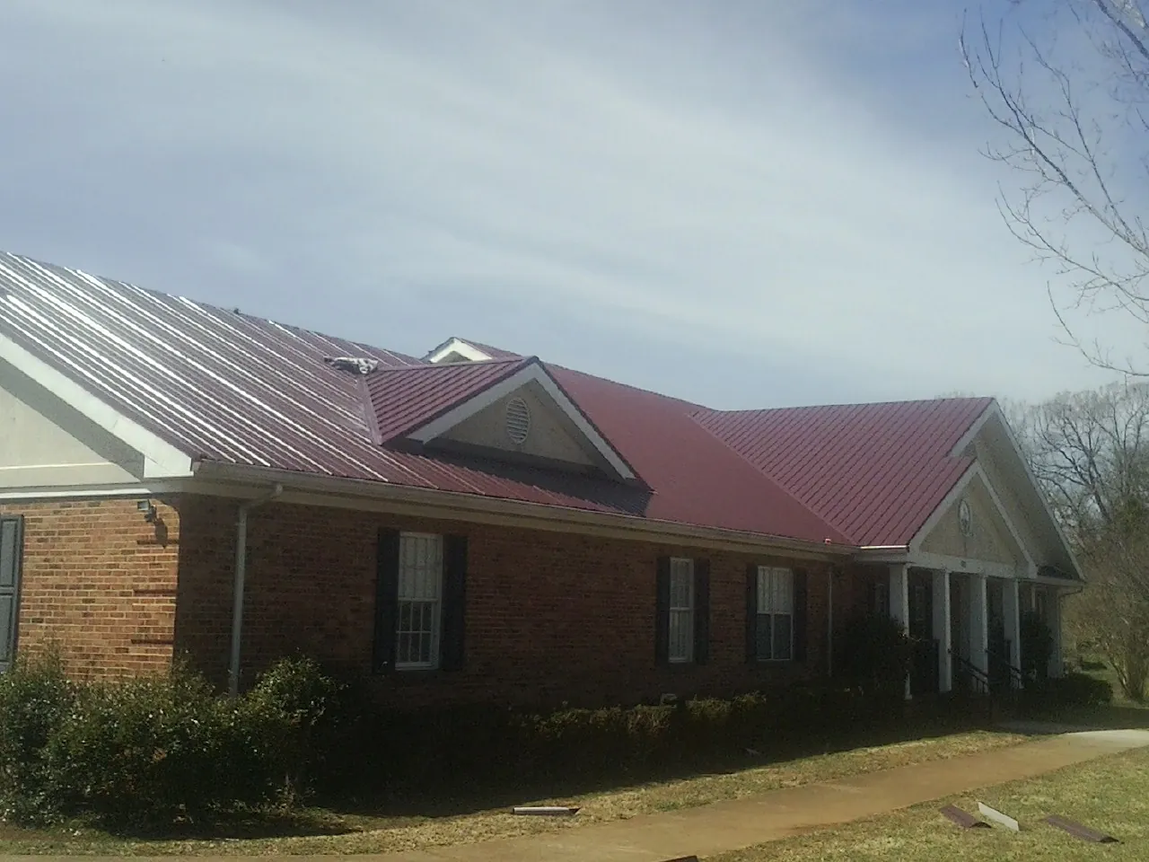 Red metal roof with gabled entries on a long brick building, from a Hail Damage Roof Repair job in Narvon