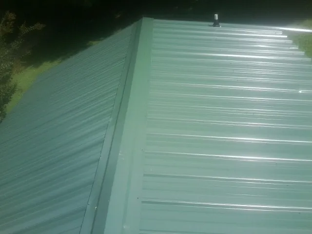New green metal panels meeting at the ridge of a roof — Flat Roof Repair work by our crew in Narvon