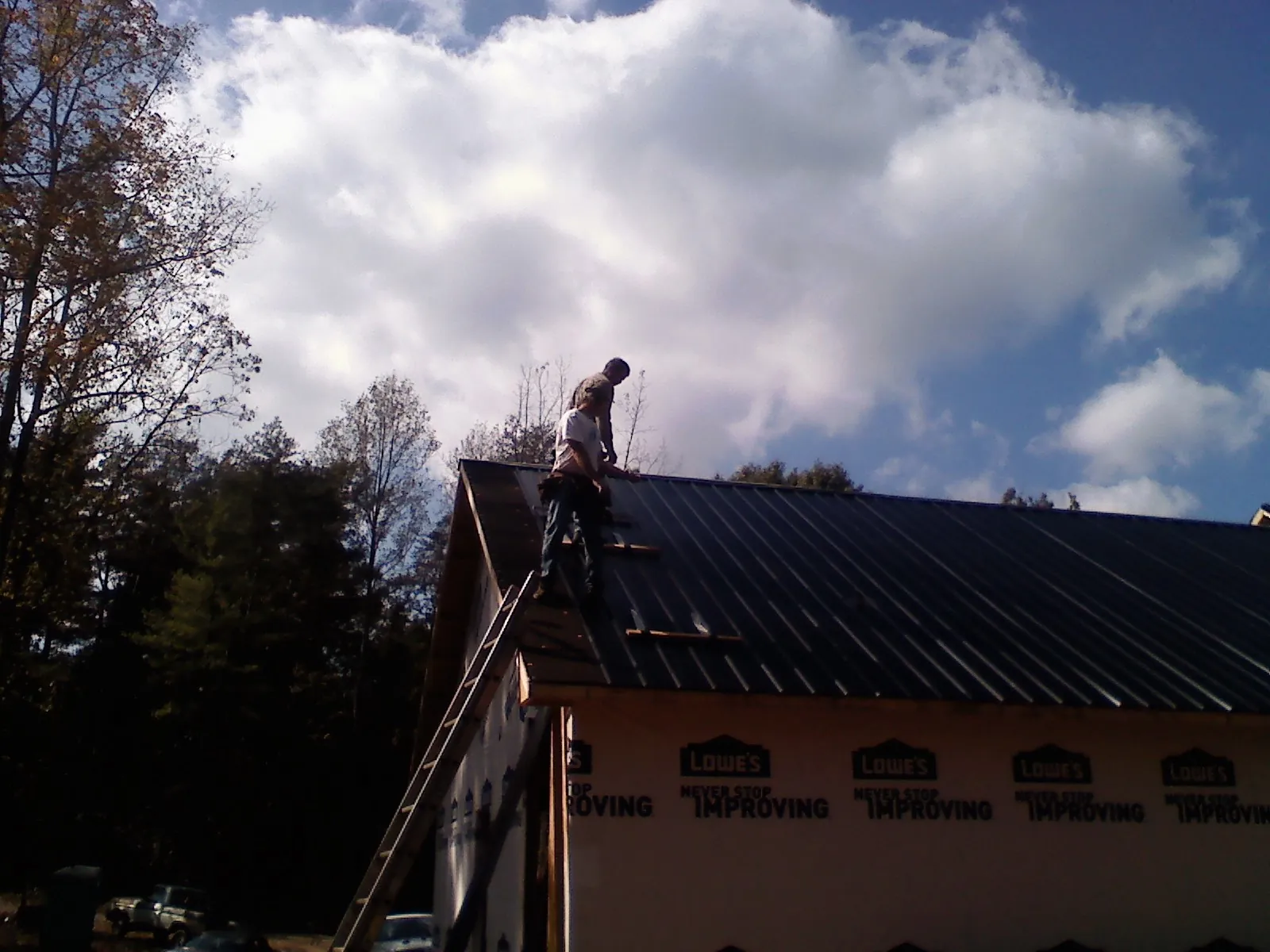 Roofer fastening dark metal panels high against a cloudy sky, from a Roof Inspection job in Narvon
